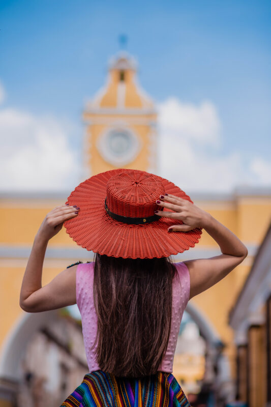 Woman wearing crimson-red wide-brim handwoven recycled-plastic Springfield Hat in front of Santa Catalina Arch in Antigua Guatemala