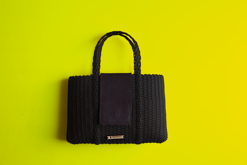 Black structured handwoven recycled plastic handbag with leather flap closure and Garments Guatemala metal plaque for European wholesale fashion buyers
