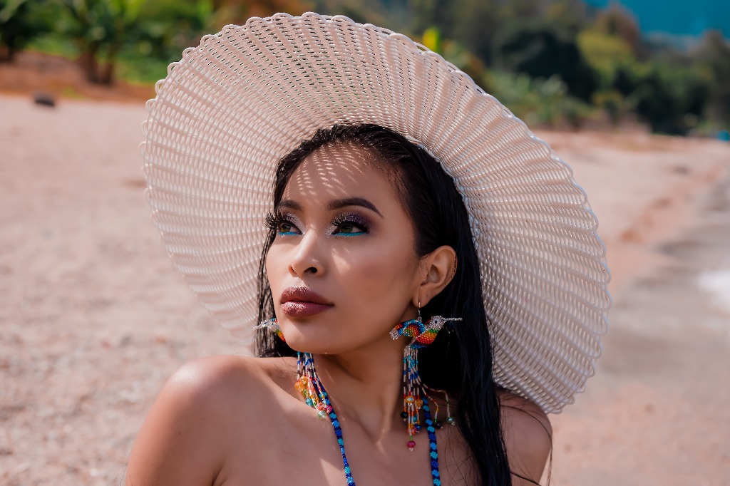 Model on a sunlit beach wearing an oversized white handwoven recycled plastic wide-brim resort sun hat crafted by Garments Guatemala